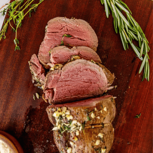 Sliced beef tenderloin with garlic and herbs on a wooden board.
