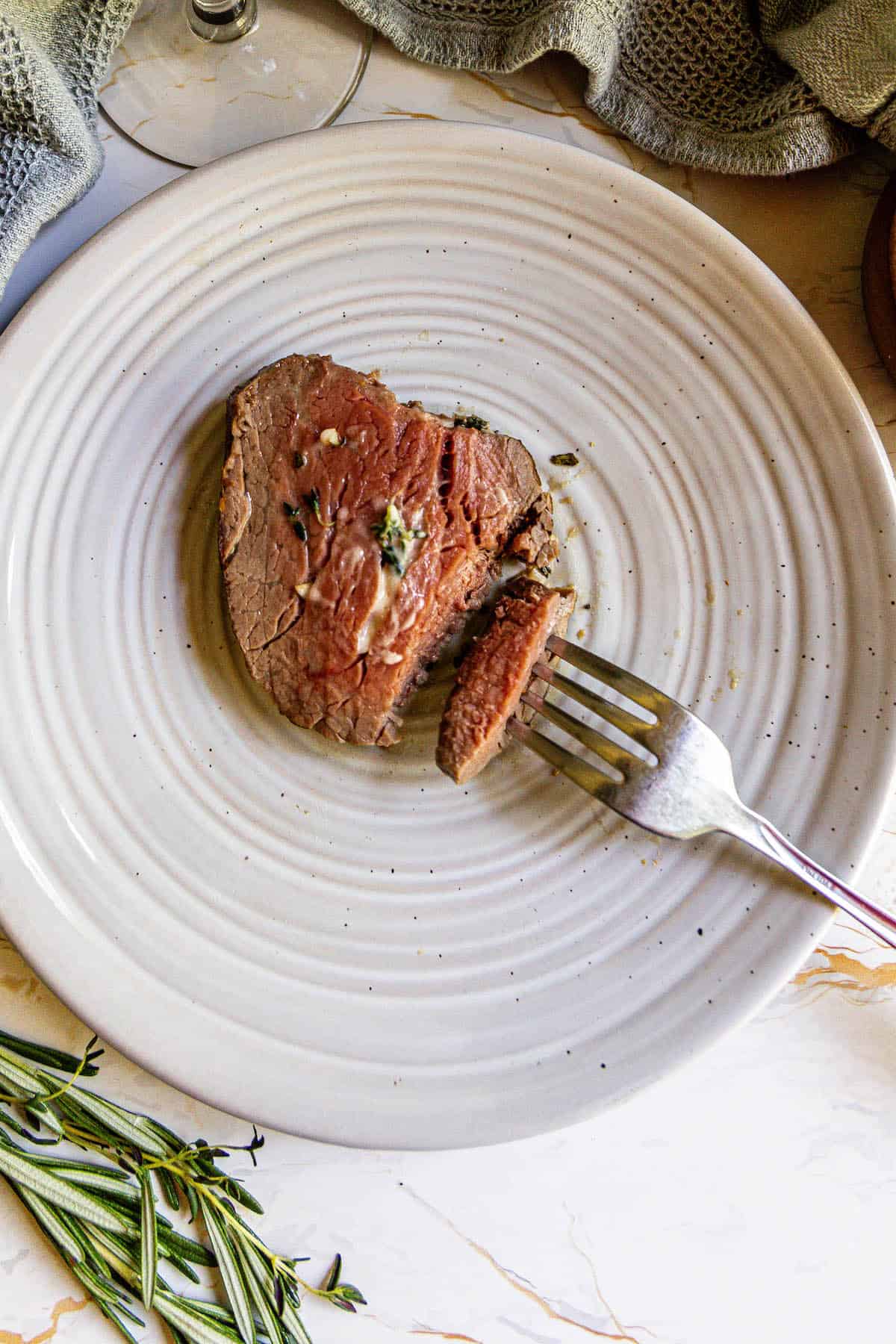 A garlic herb beef tenderloin on a plate with a fork.