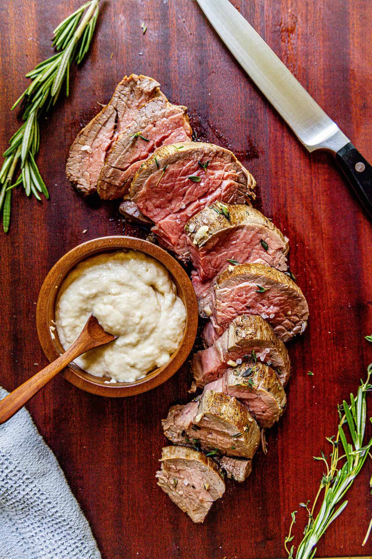 A garlic-infused beef tenderloin on a cutting board, garnished with sprigs of rosemary.
