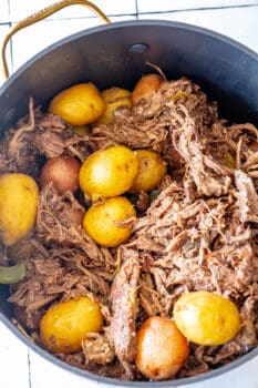 A pot roast simmering with meat and potatoes in a pan.