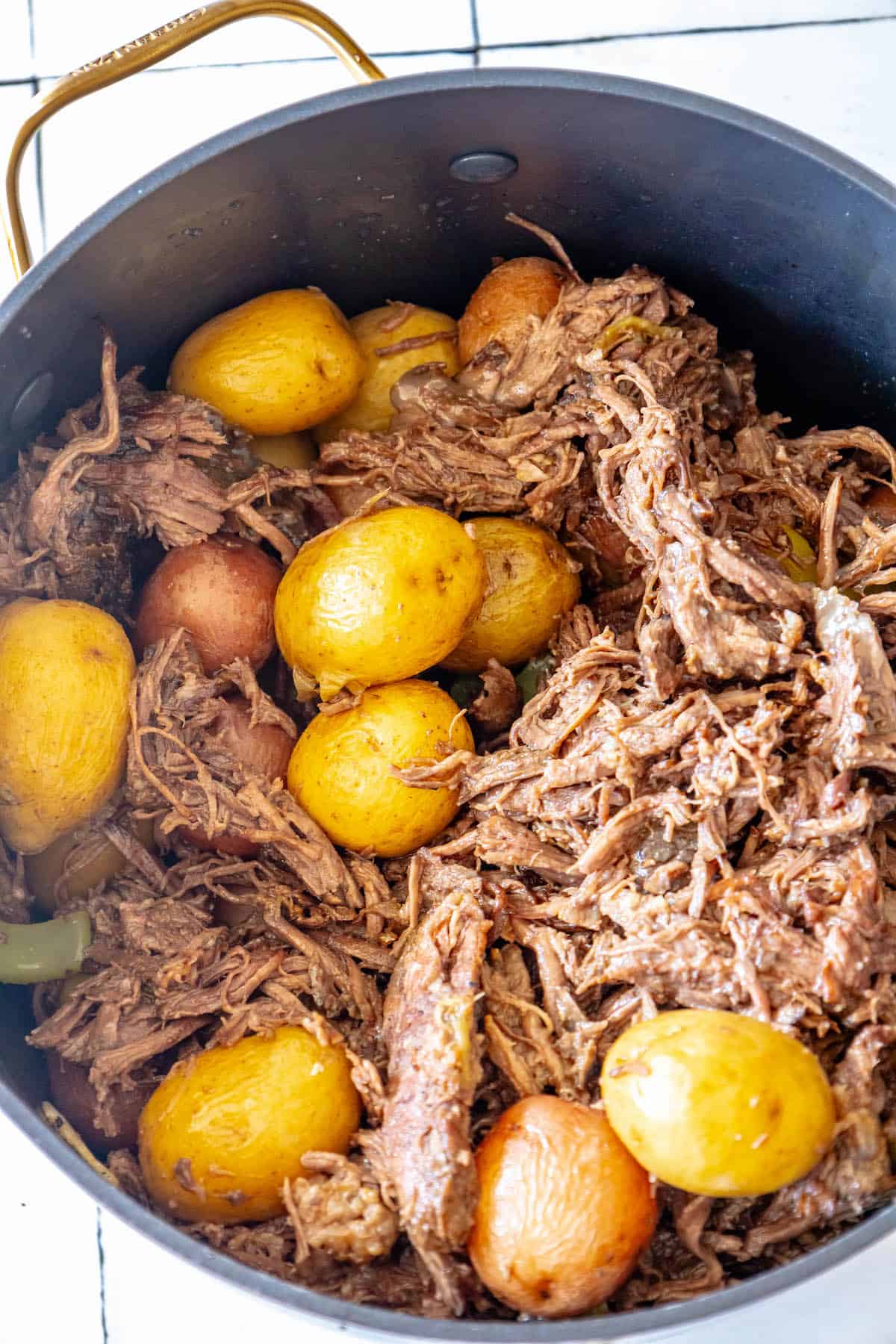 A pot roast simmering with meat and potatoes in a pan.