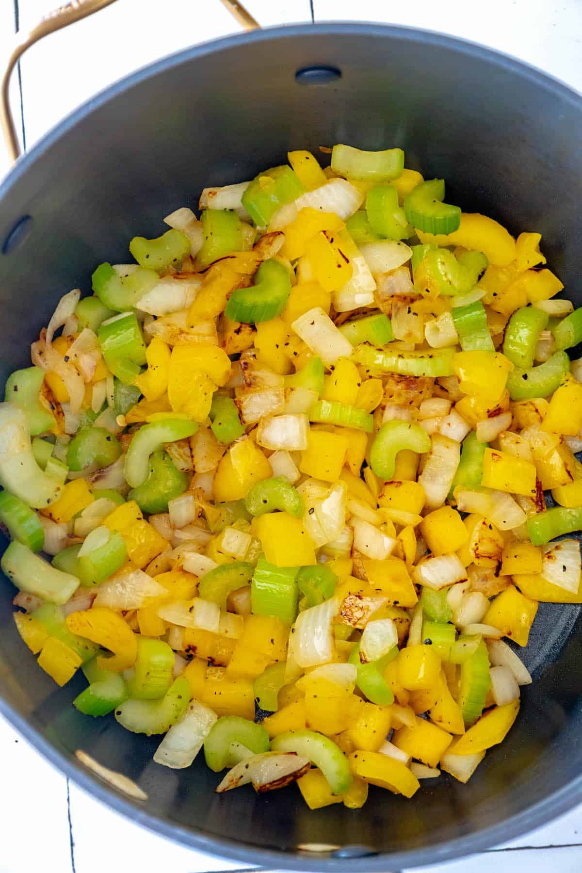 A pot full of yellow and green peppers and onions prepared for a delightful soup.