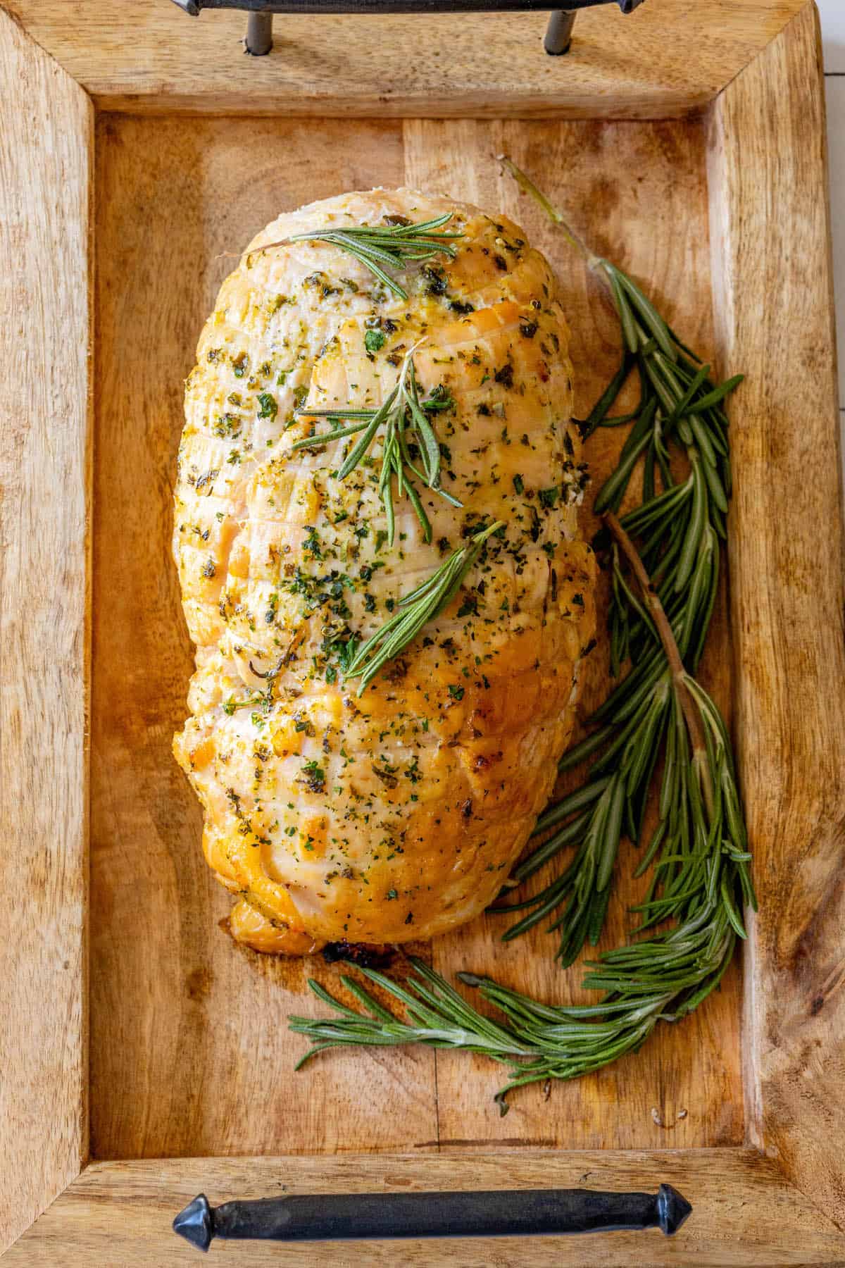 An Oven Baked Turkey Breast with rosemary on a wooden tray.