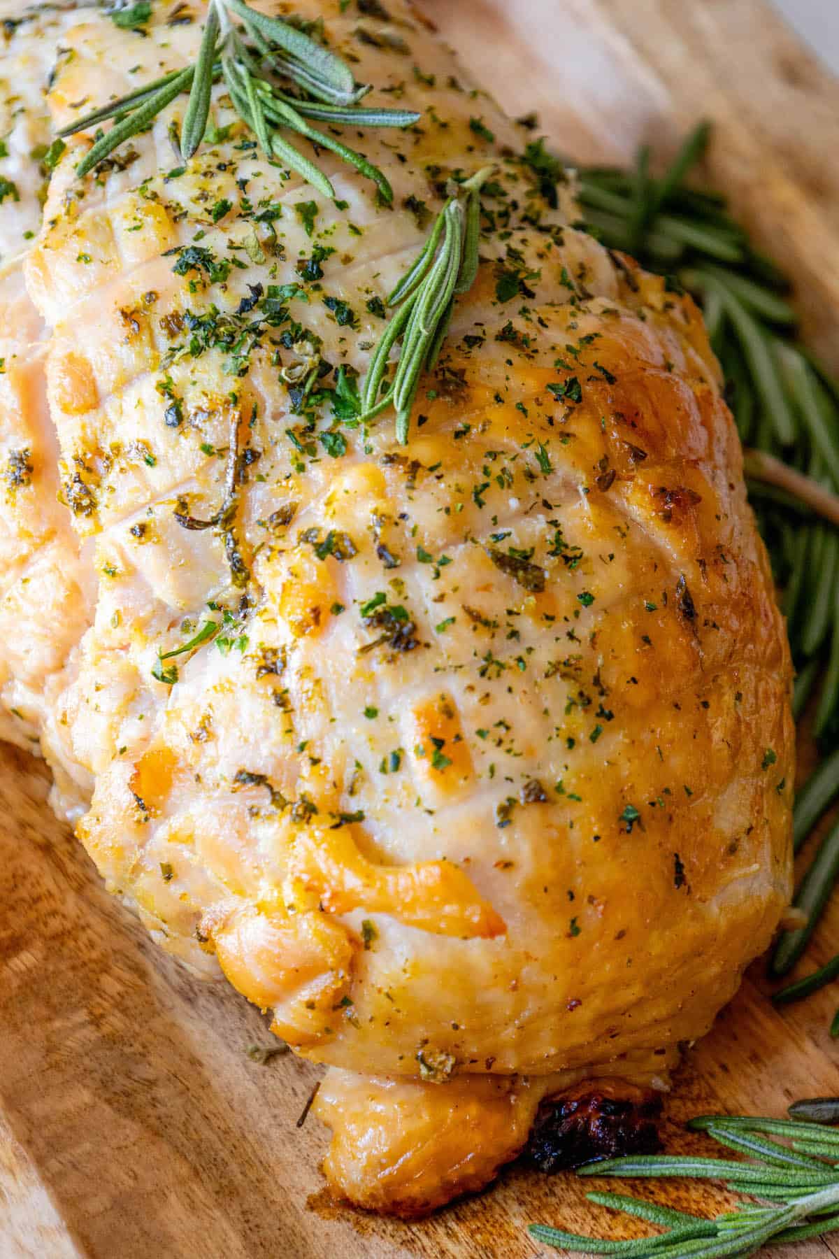 A roasted turkey on a cutting board with sprigs of rosemary. Oven Baked Turkey Breast.