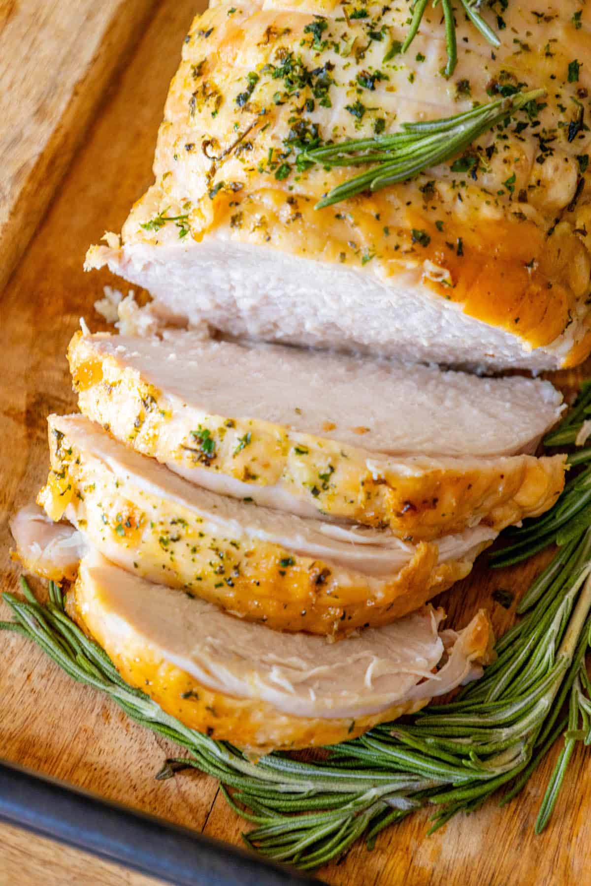 Sliced turkey with rosemary on a cutting board, showcasing an easy and delicious turkey breast recipe.