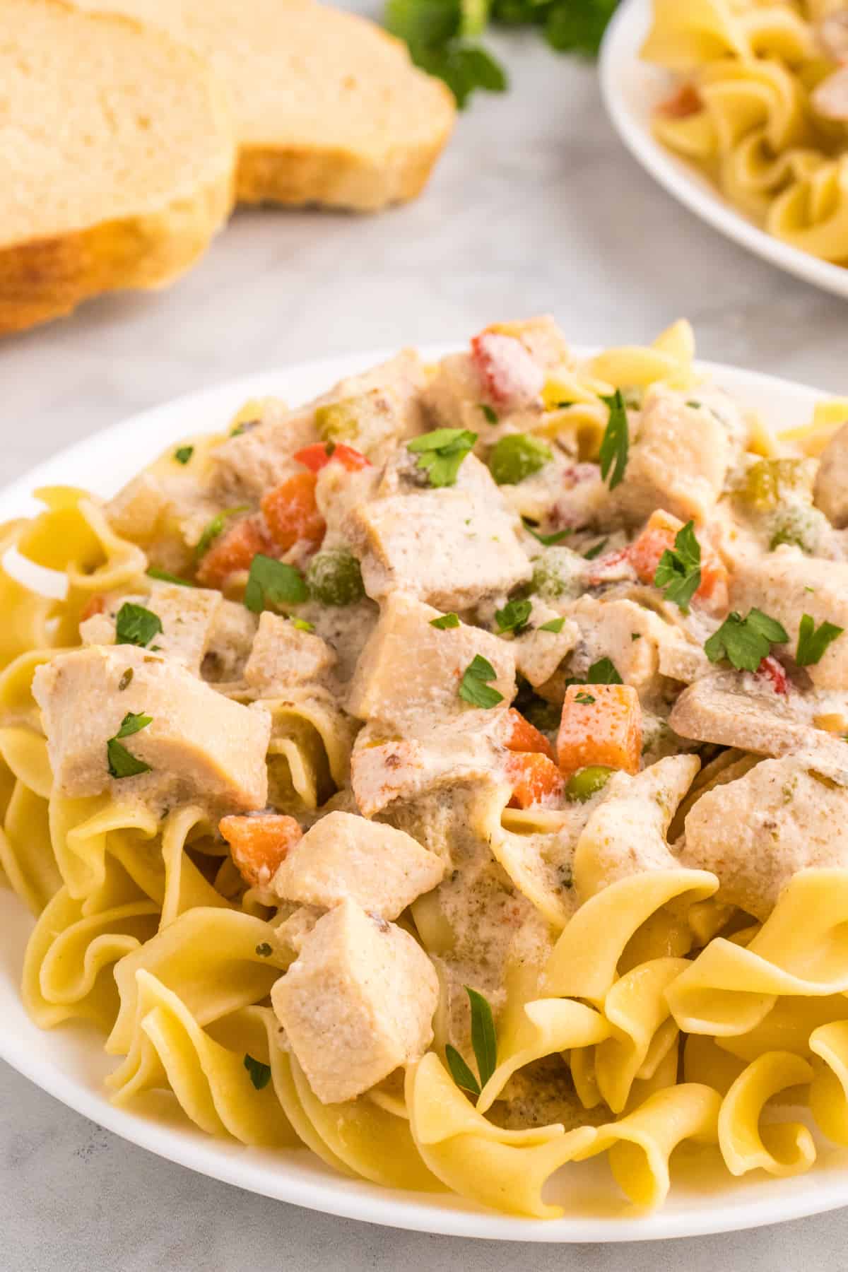 A slow cooker chicken a la king with vegetables served over a plate of pasta.