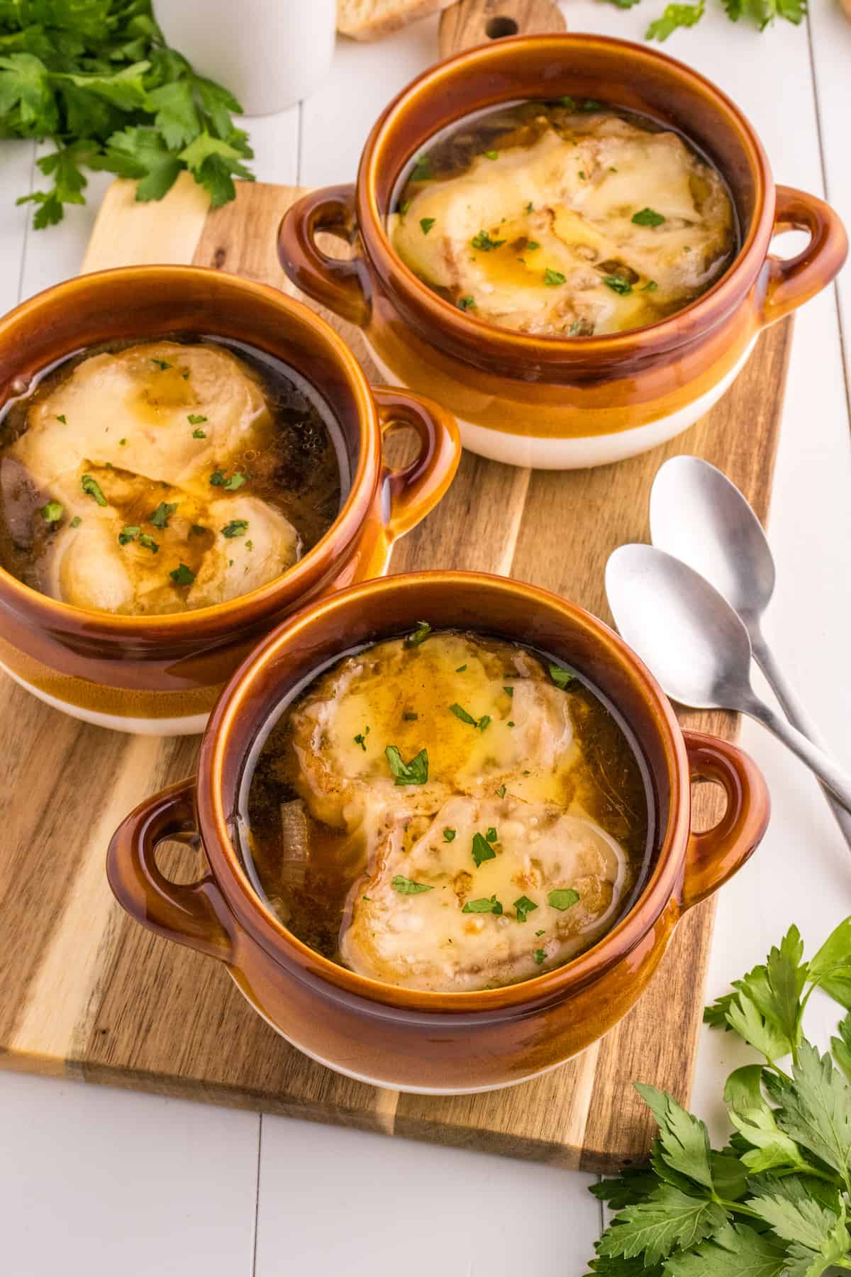 The Best French Onion Soup Recipe - Three bowls of easy french onion soup on a wooden cutting board.