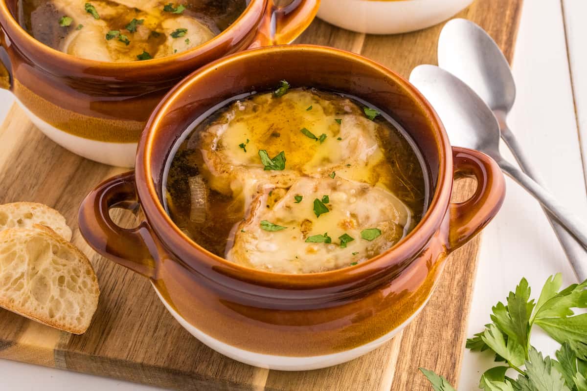 Two bowls of the best French onion soup recipe on a wooden cutting board.