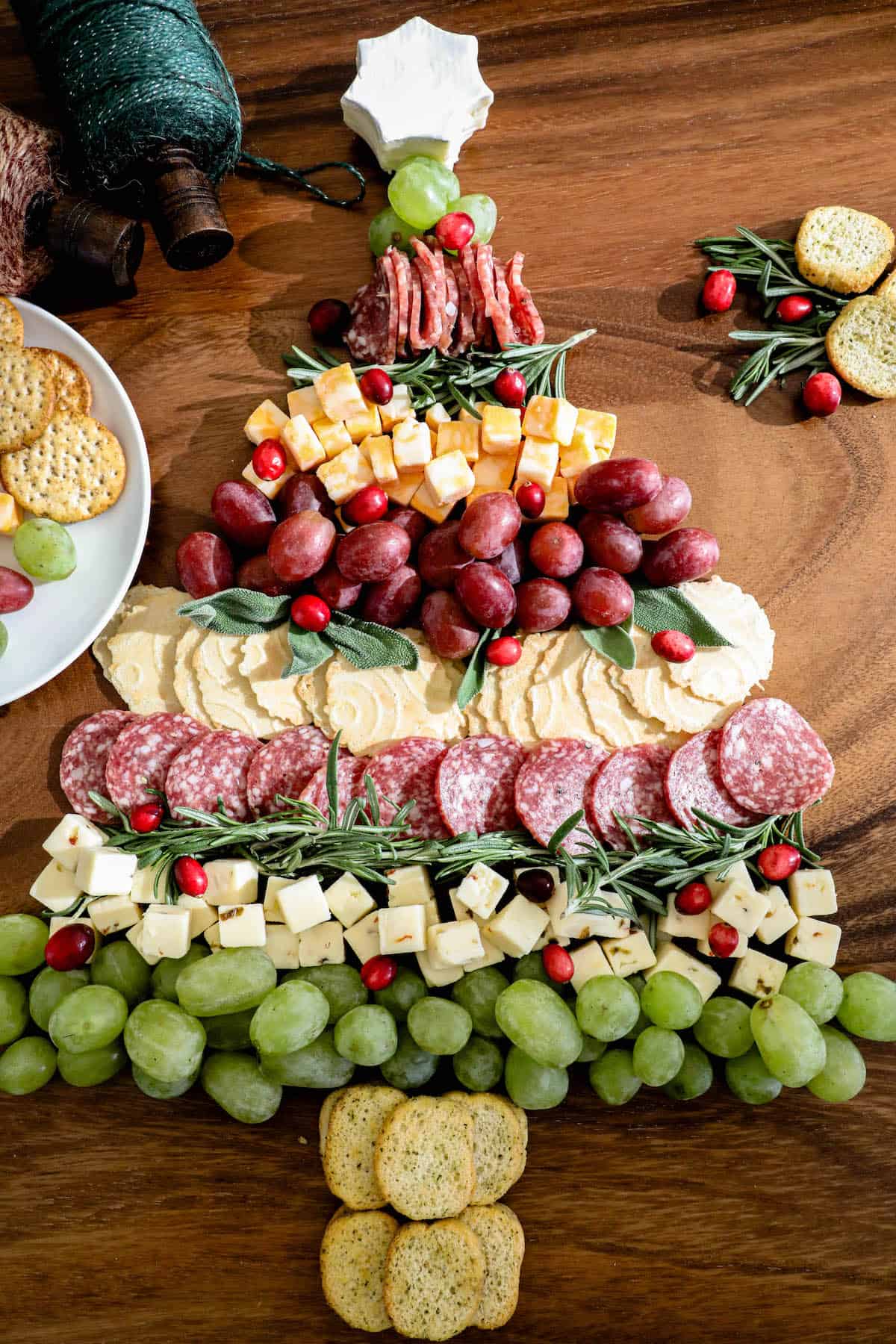 A festive Christmas cheese board adorned with a delightful assortment of crackers, grapes, and a cheese Christmas tree centerpiece.