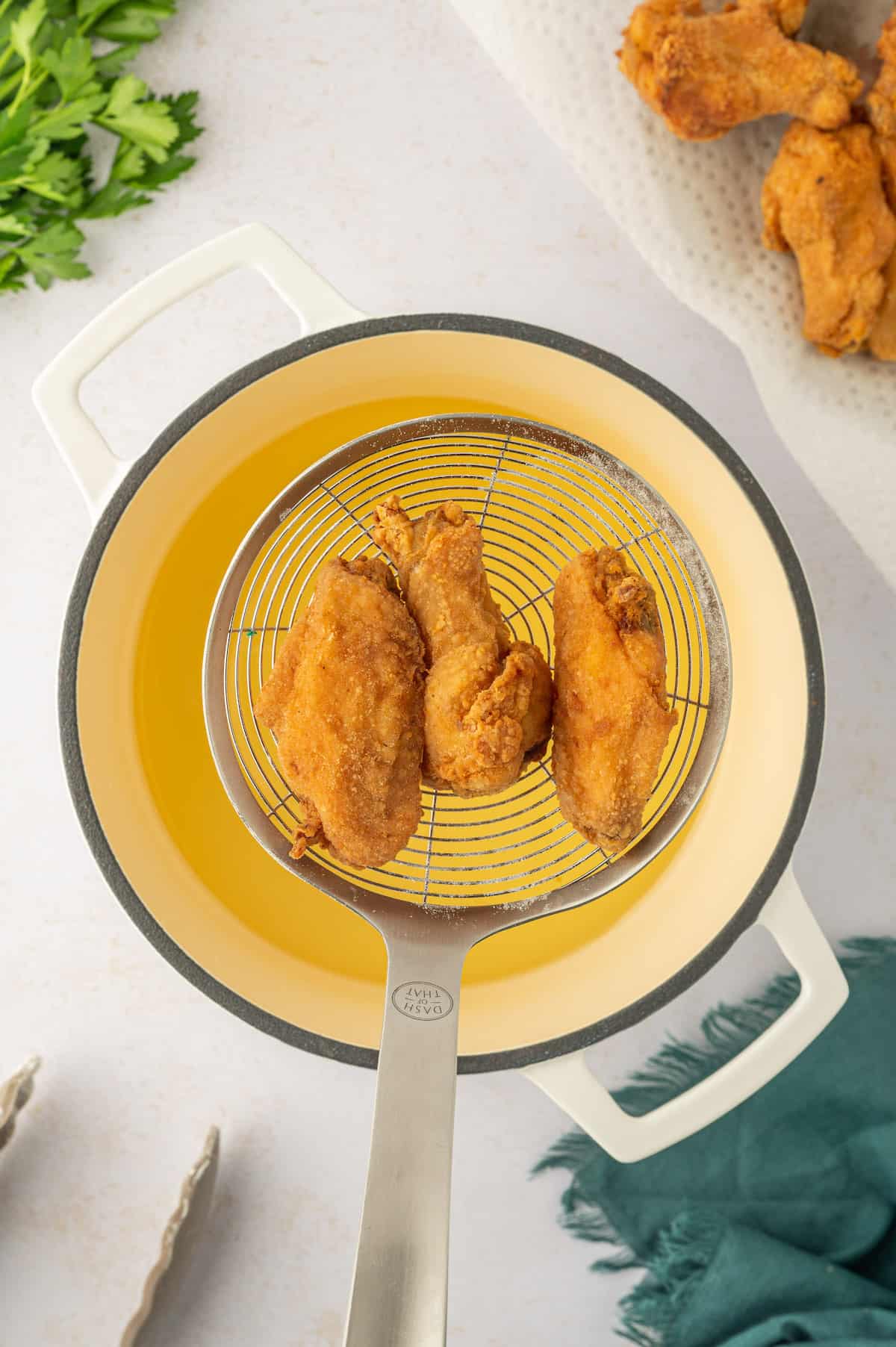 Chicken wings with a lemon pepper seasoning, cooked in a yellow pan with a spatula.