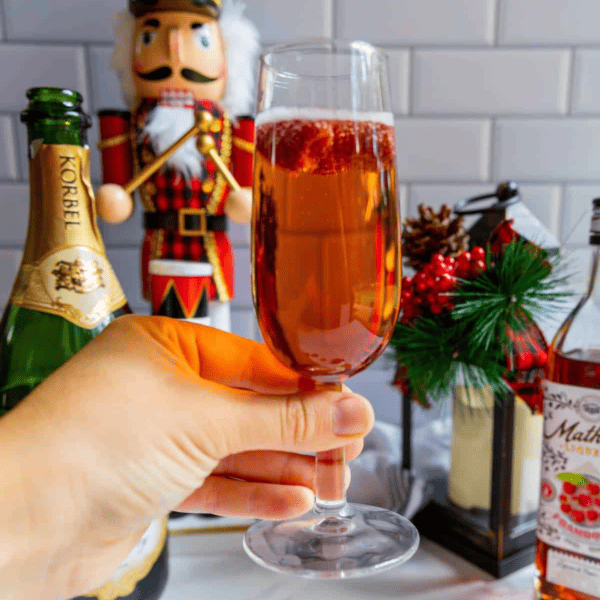 A person holding a glass of raspberry champagne in front of a nutcracker.