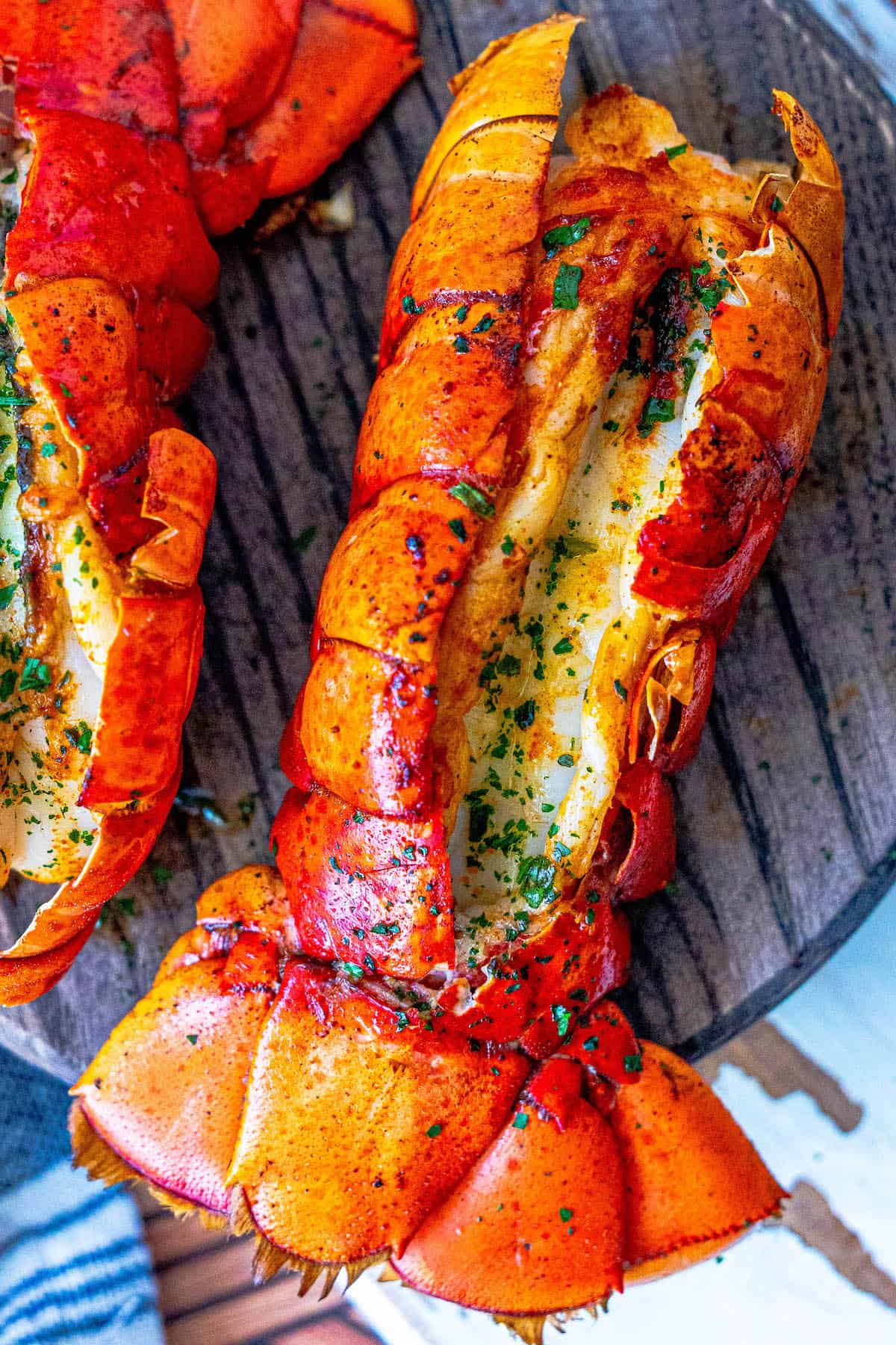 Two broiled lobster tails on a wooden board.