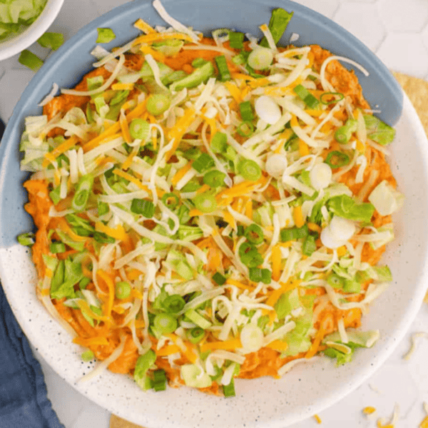 A bowl of cheesy nacho dip with shredded cheese and tortilla chips.