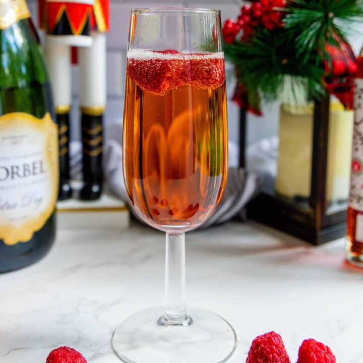 A glass of raspberry champagne sparkler with raspberries and a bottle of champagne.