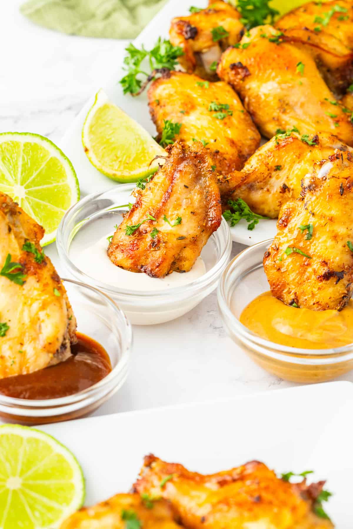 Air fried chicken wings with sauce and lime wedges on a white plate.