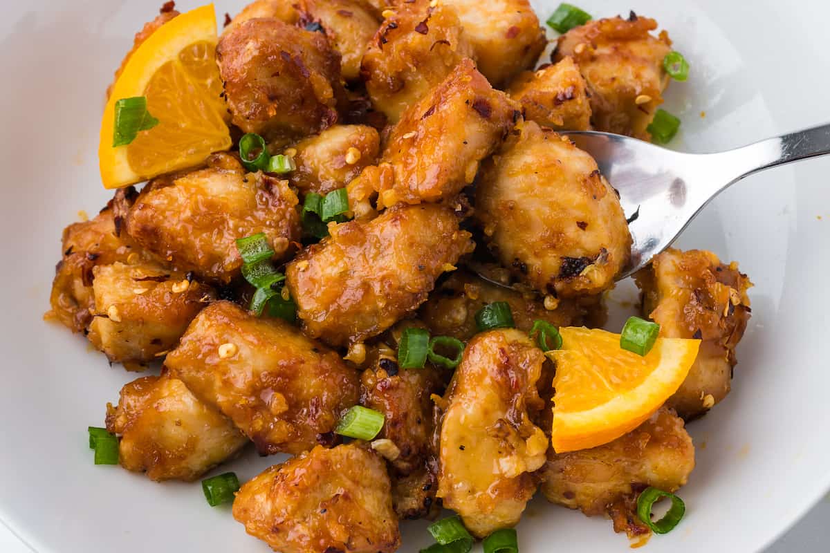 A bowl of orange chicken from the air fryer, with a fork.
