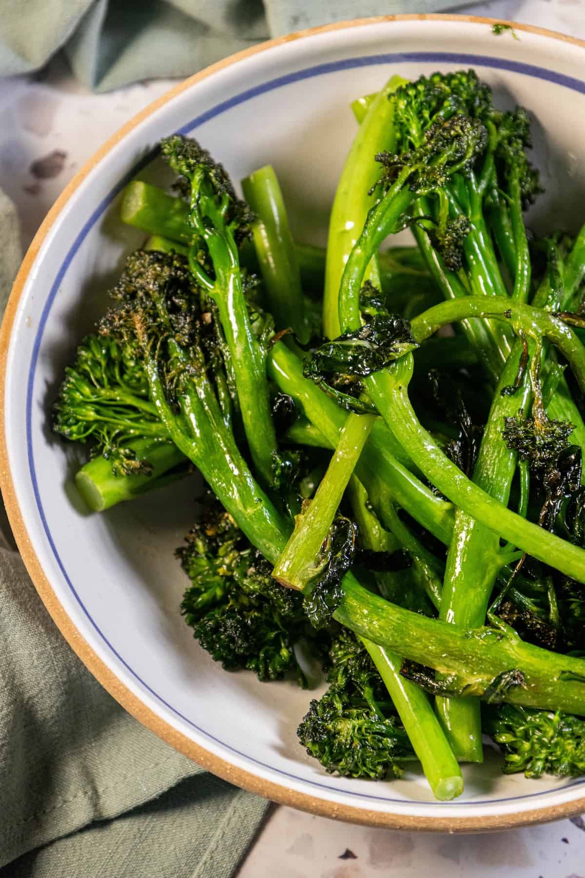 A bowl of sauteed broccolini on a table with a napkin.