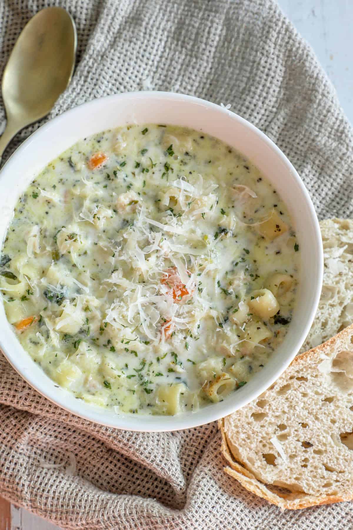 A creamy chicken noodle soup with bread next to it.