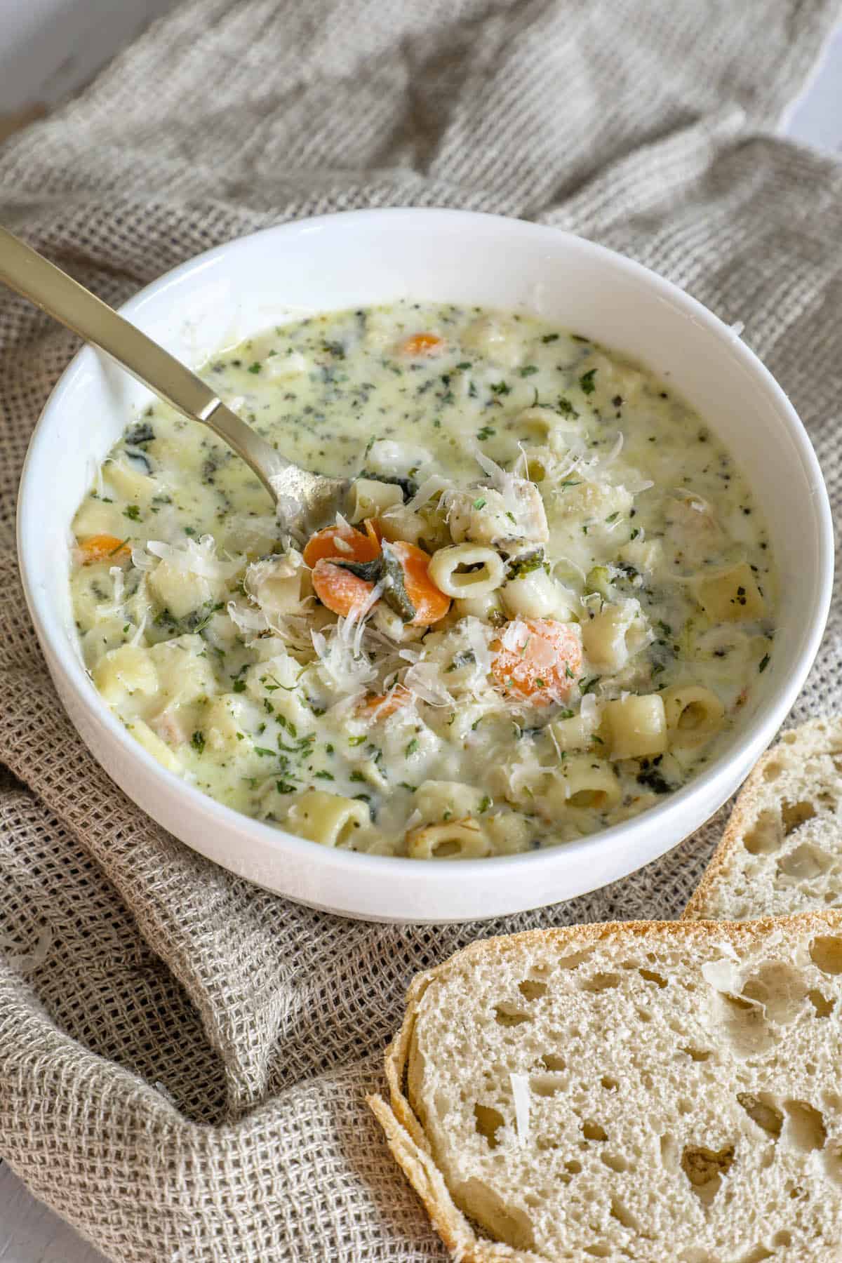 A creamy bowl of chicken noodle soup with bread next to it.