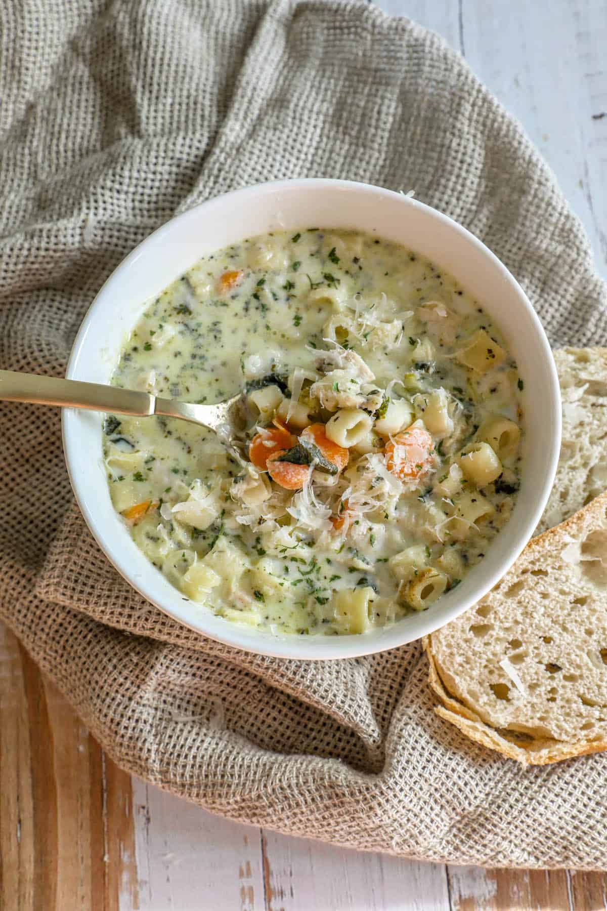 A creamy bowl of chicken noodle soup with bread on top.