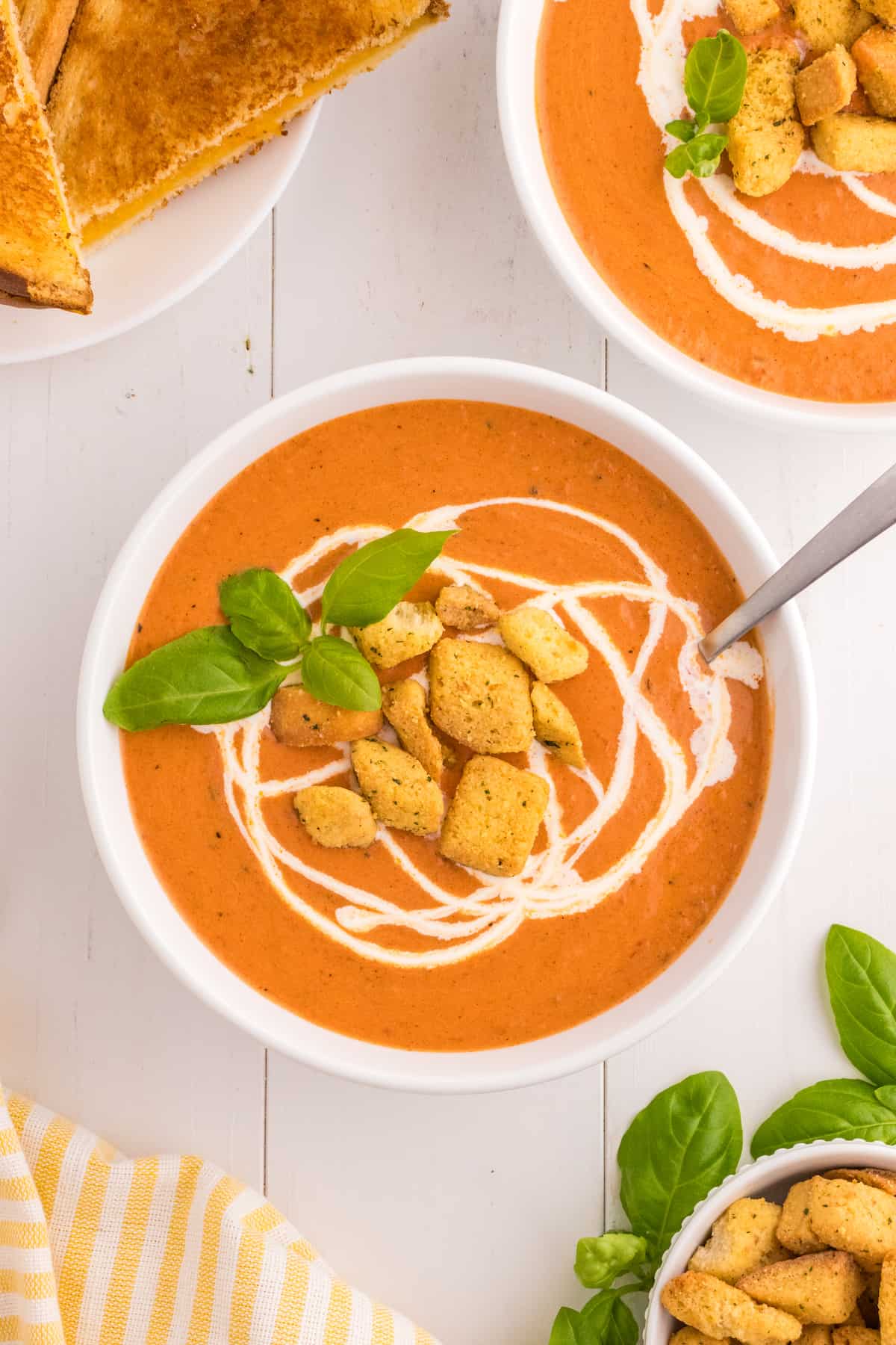 Two bowls of tomato soup with croutons and basil.