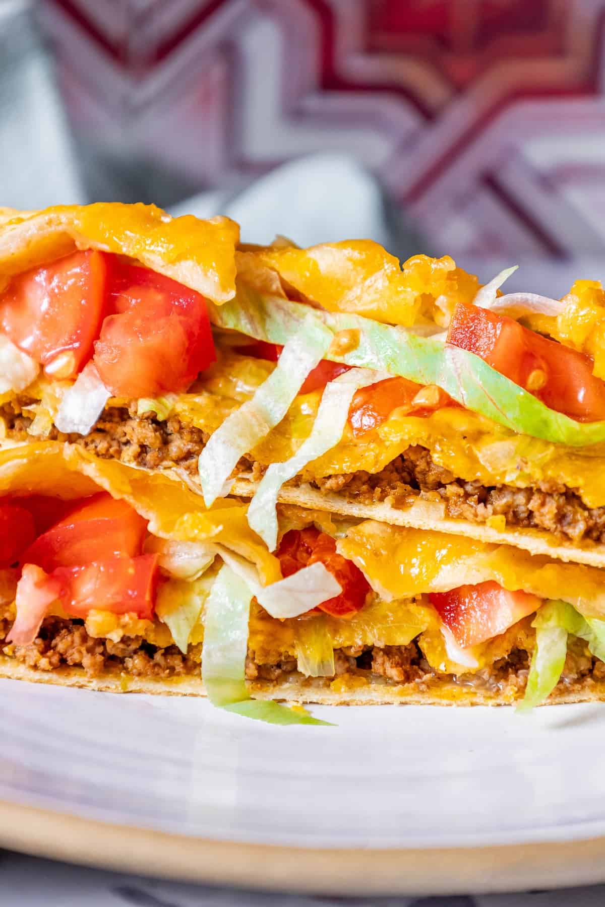 A stack of CrunchWrap tacos on a plate with tomatoes and lettuce.