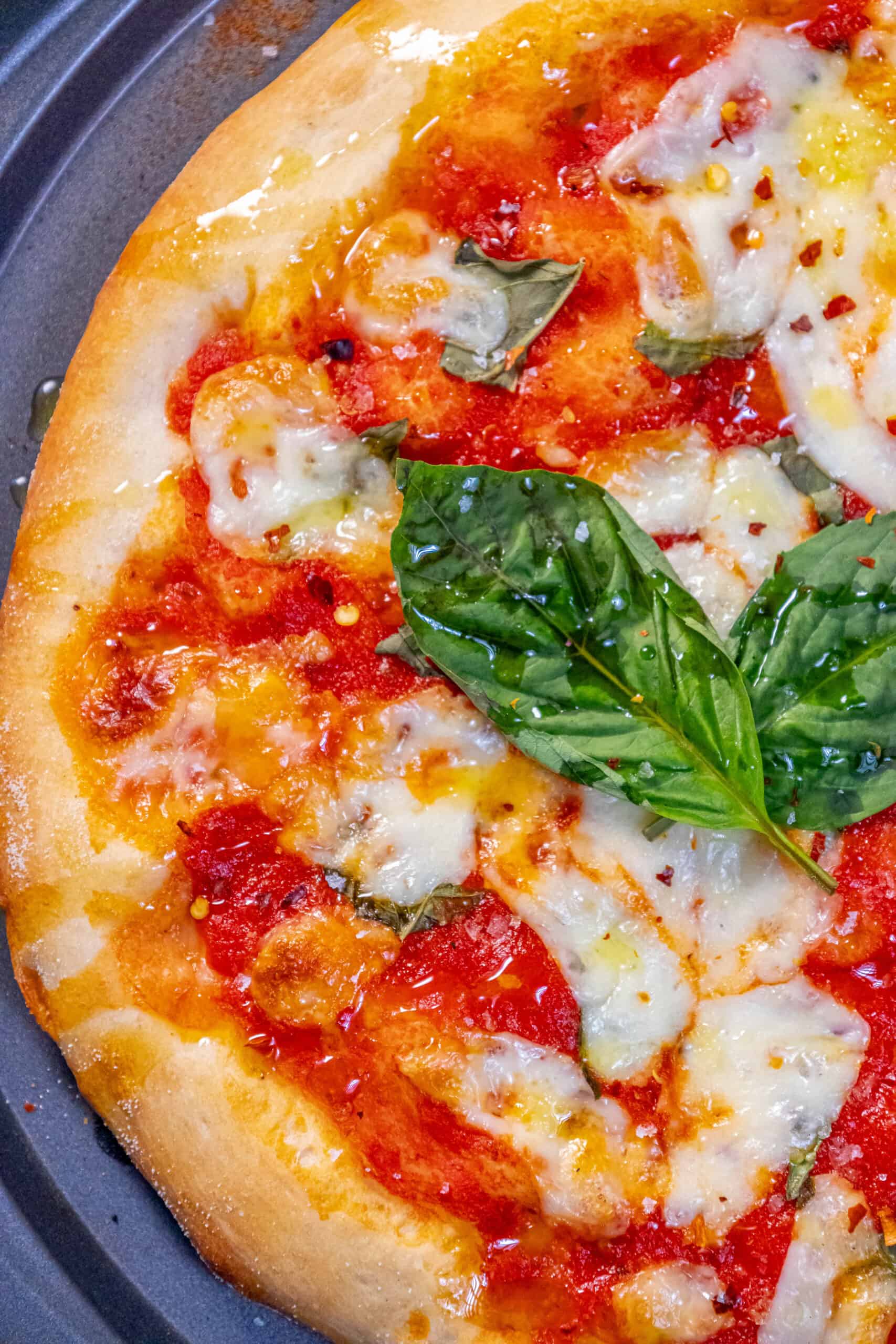 A Margherita pizza on a pan with a basil leaf and sauce.