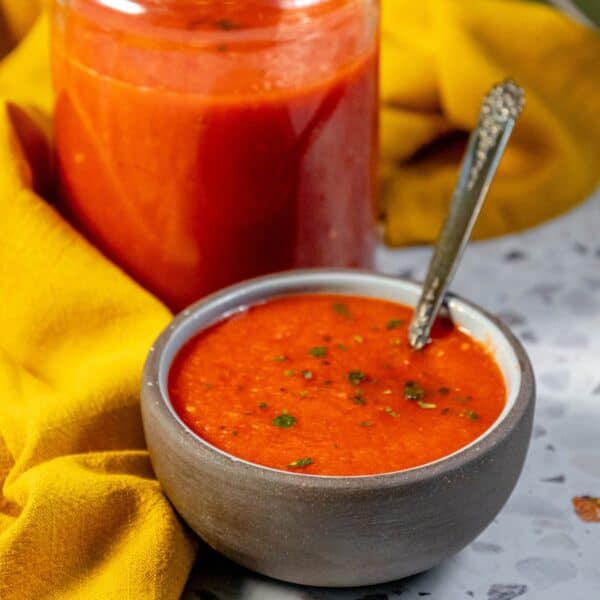 A bowl of tomato soup with Margherita pizza sauce and a spoon next to a jar.