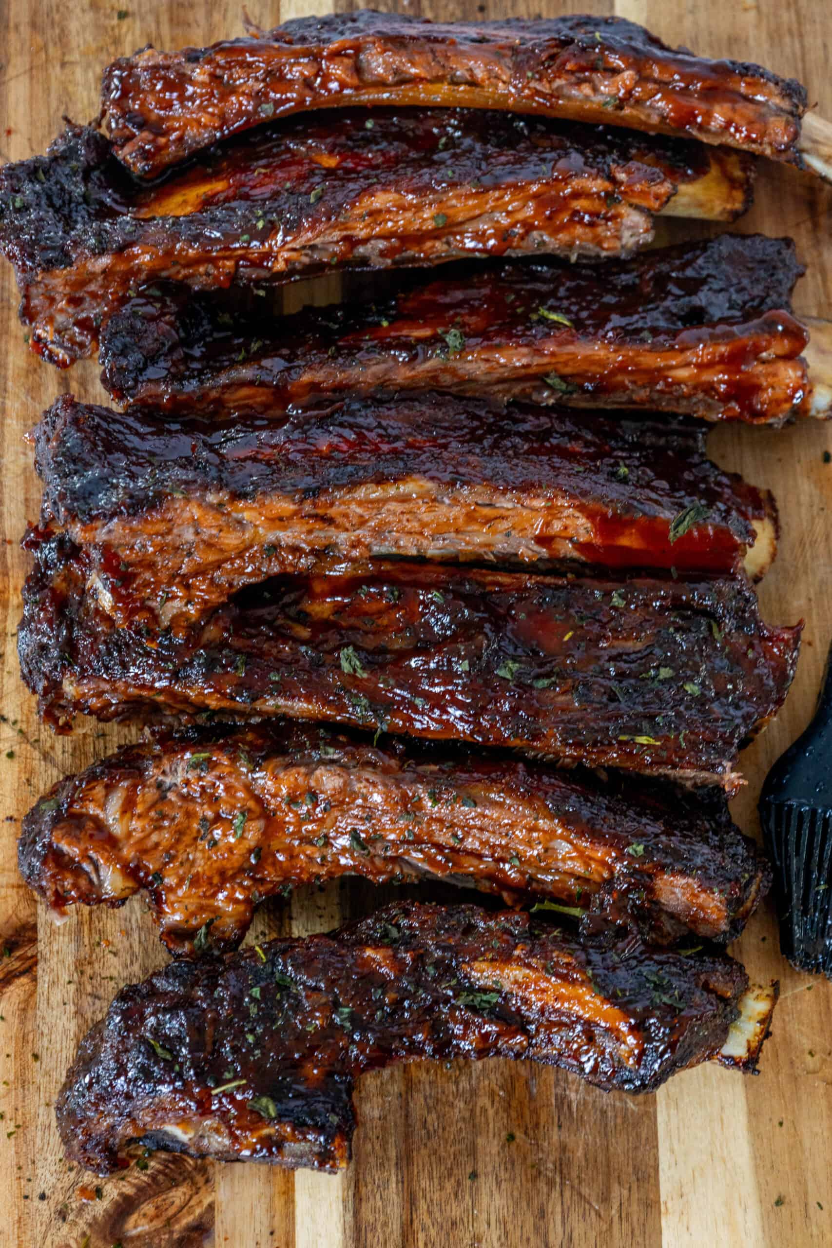 Oven baked BBQ beef ribs on a wooden cutting board.