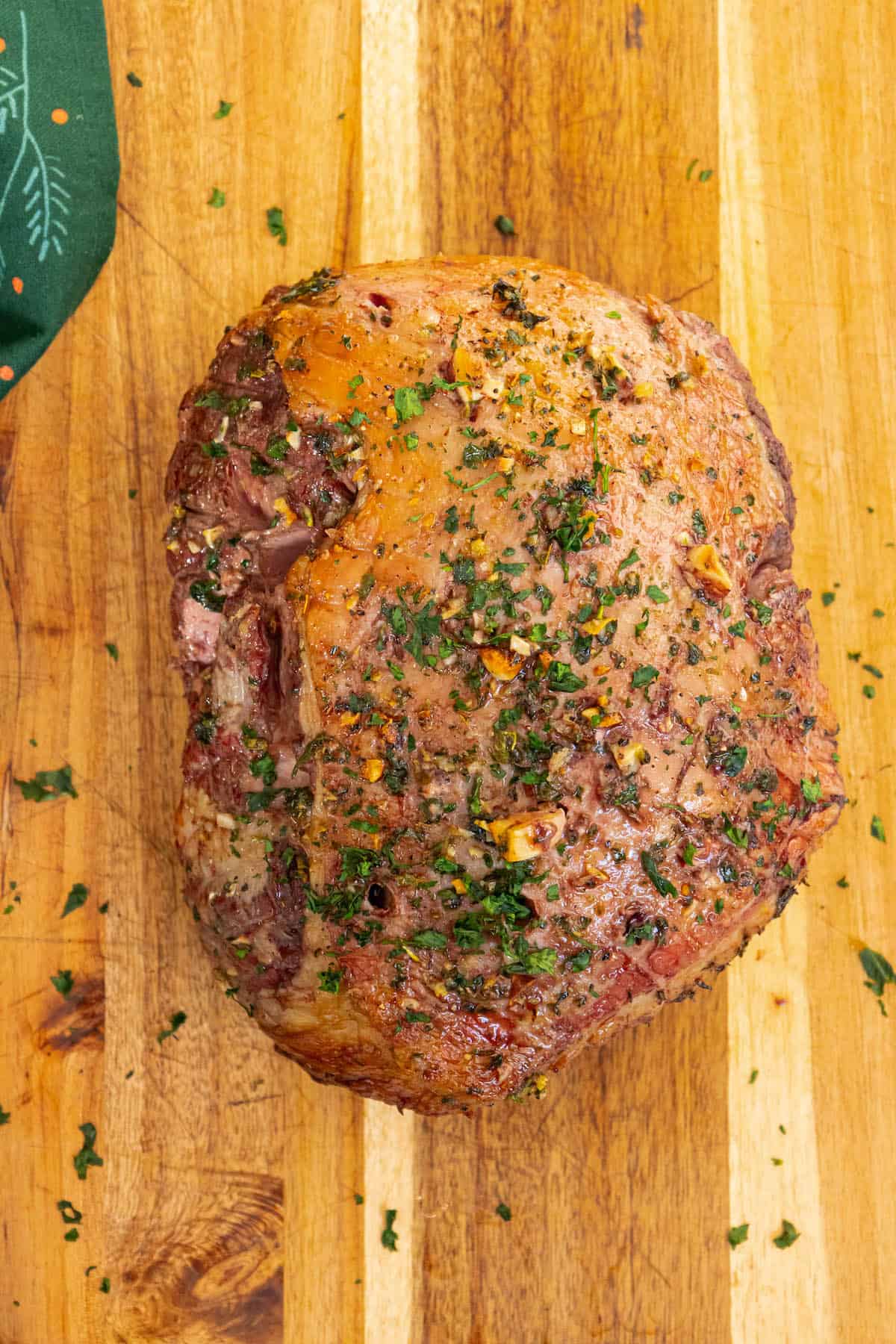 A Reverse Seared Leg of Lamb with herbs on a wooden cutting board.