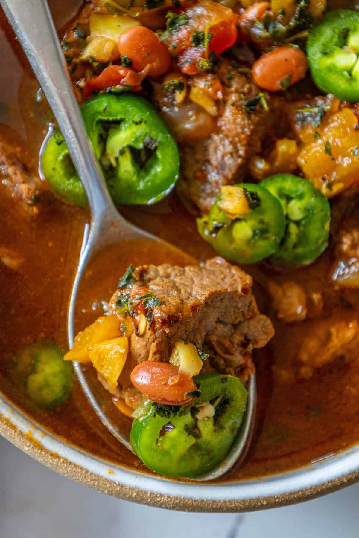 Spicy stew with meat and jalapeño peppers in a bowl.