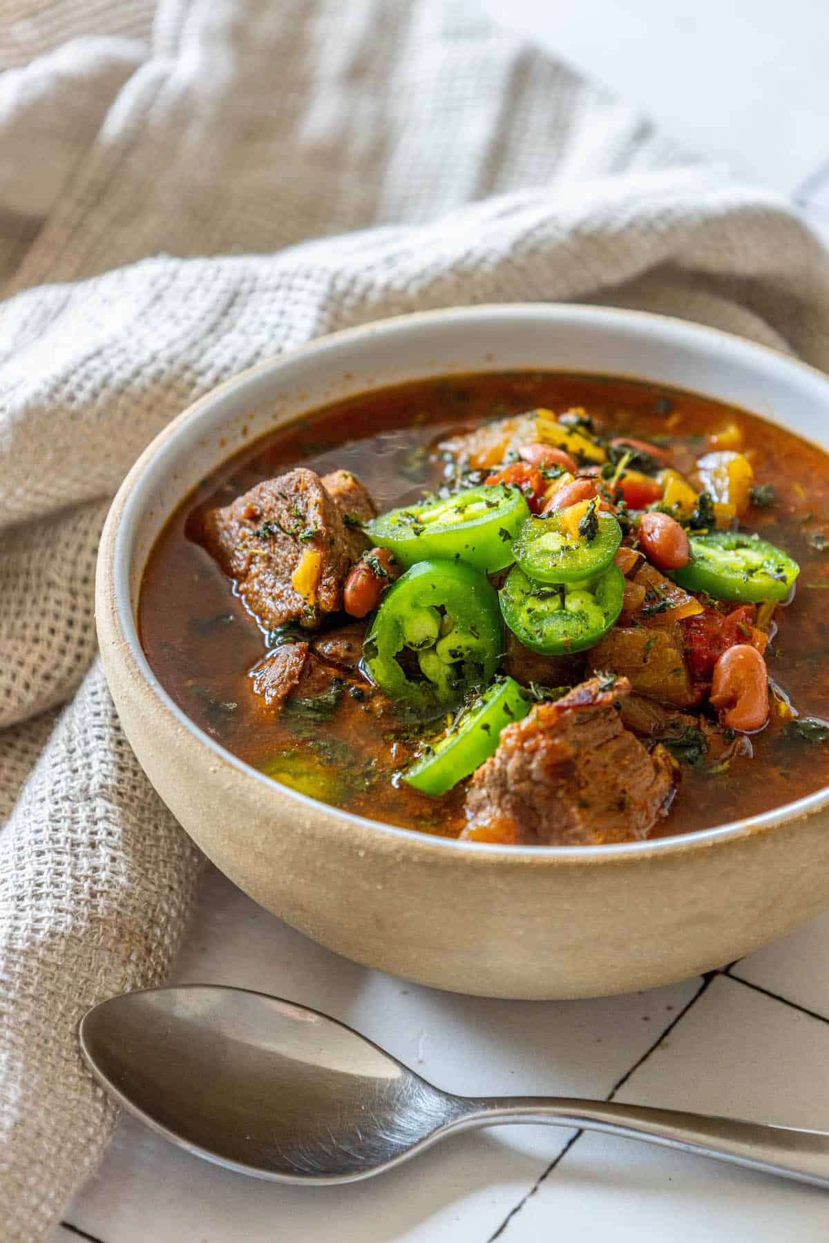 A bowl of spicy beef soup with vegetables and jalapeños.
