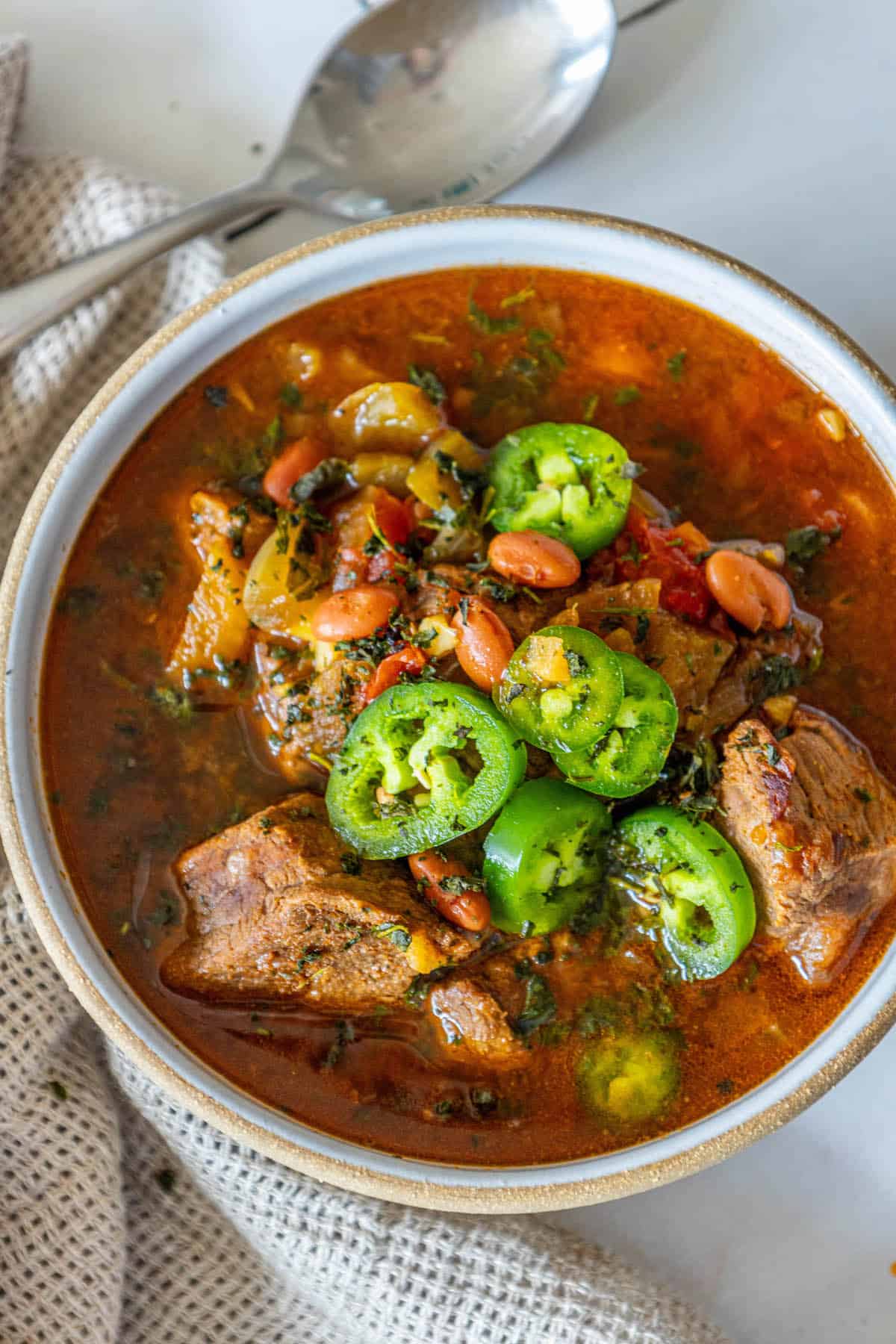 A bowl of stew with meat, beans and jalapenos.