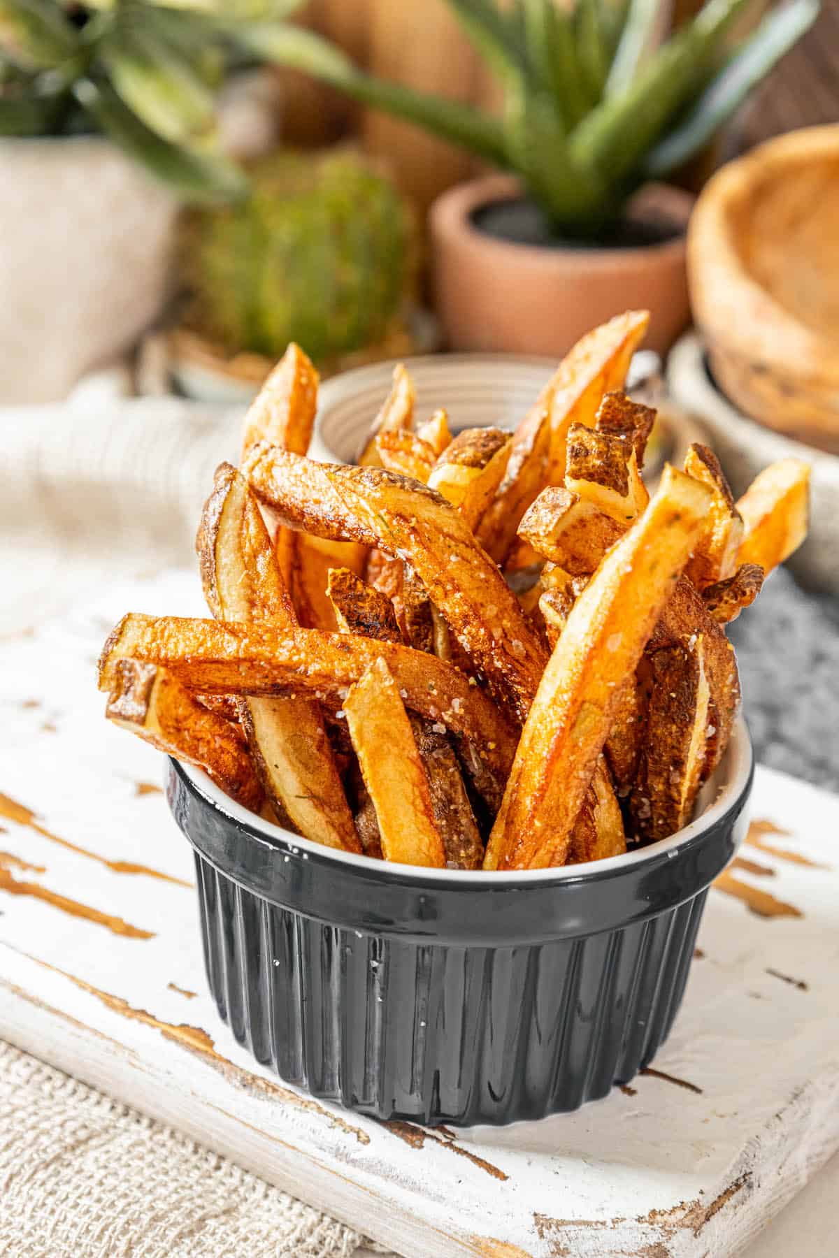 Air fryer french fries in a bowl on top of a wooden cutting board.