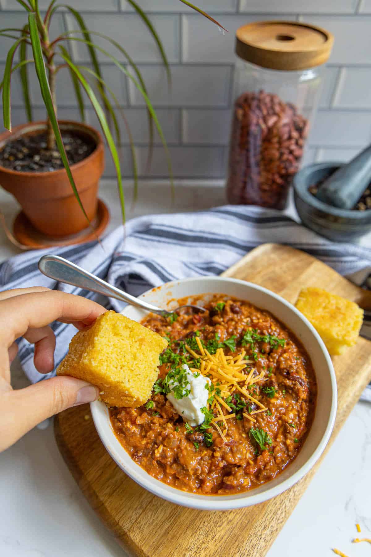 A bowl of chili with cornbread on a wooden cutting board.