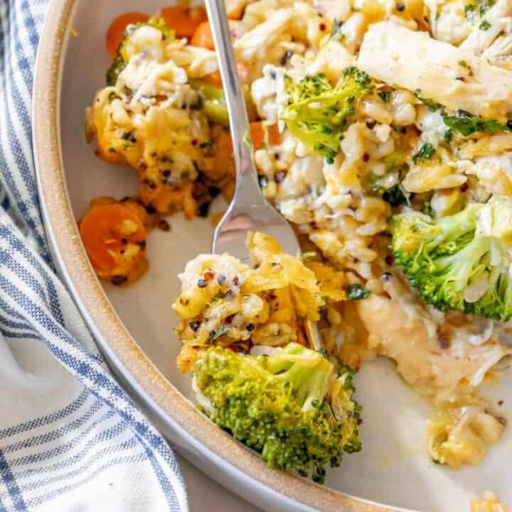 A plate of cheesy chicken and broccoli with a fork.