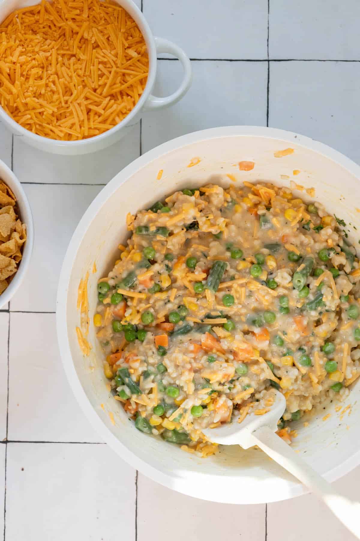 A bowl of mashed potatoes, peas, carrots and cheesy cheese.