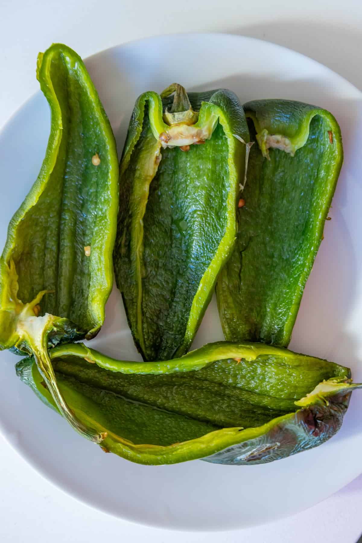 Three green peppers on a white plate, prepared as Chile Rellenos.