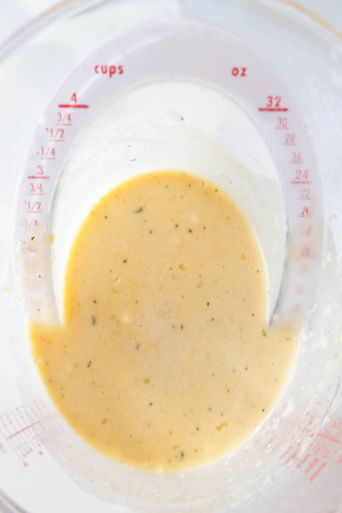 A skillet with a measuring cup filled with a yellow sauce.
