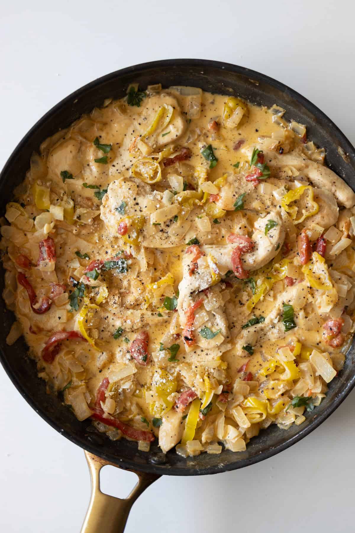 Chicken breast strips in a creamy sauce with chopped onions, yellow and red peppers, and herbs, cooked in a black skillet with a gold handle—a delicious chicken pepper creamy dinner.