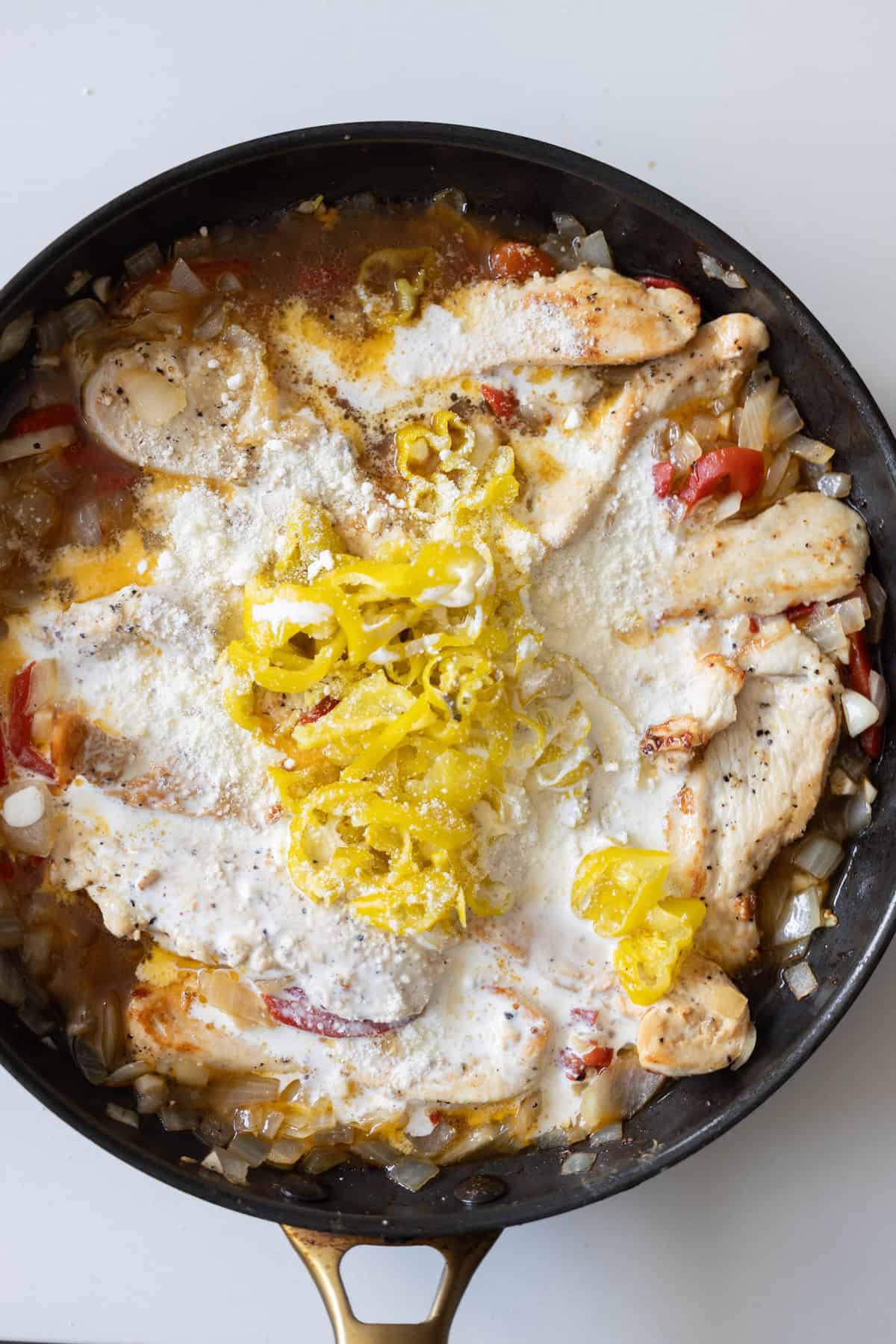 A skillet filled with cooked chicken breasts, sliced onions, tomatoes, cream, grated cheese, and yellow peppers makes a delicious Creamy Pepperoncini Chicken Skillet perfect for any dinner.