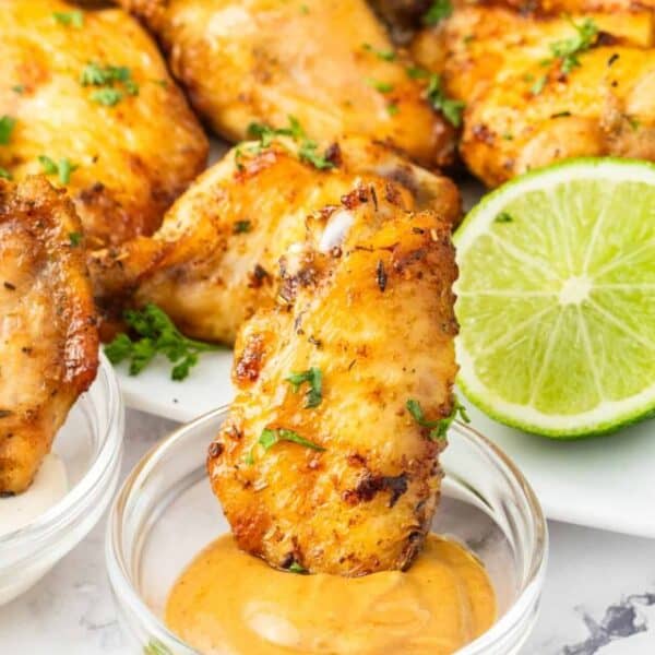 A plate of chicken wings with sauce and lime wedges.