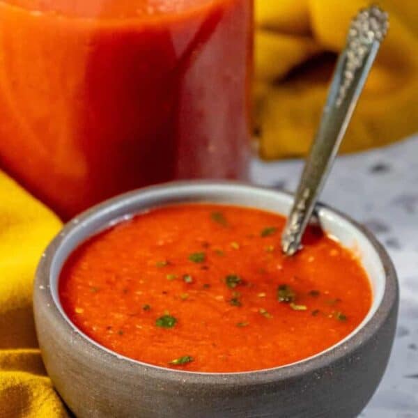 A bowl of tomato soup with a spoon next to a jar.