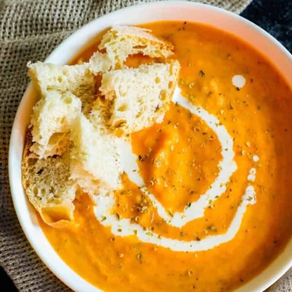 A bowl of carrot soup with a slice of bread.