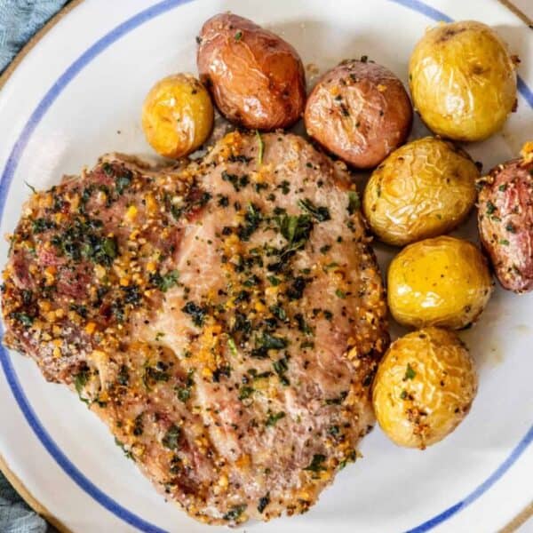 Pork chops on a plate with potatoes and herbs.