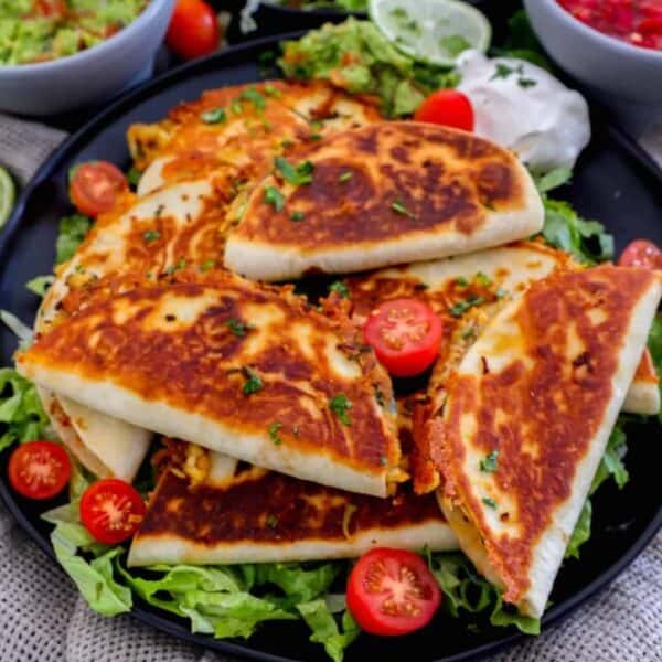Quesadillas on a black plate with tomatoes and guacamole.