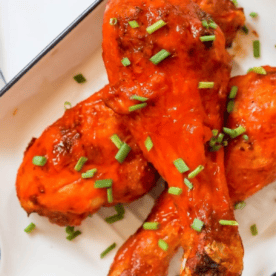 Crunchy BBQ chicken legs on a plate with green onions.