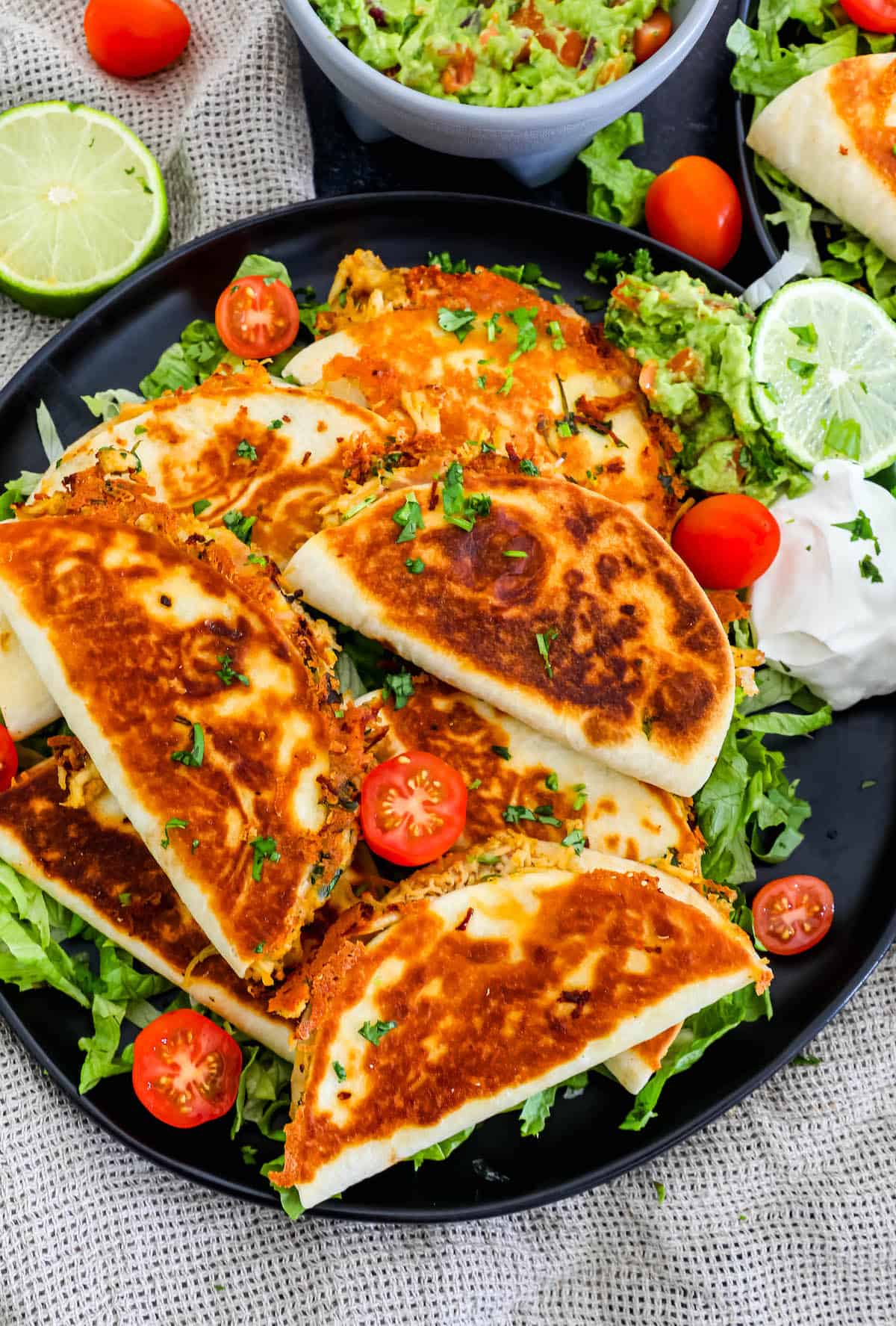 Mini chicken quesadillas on a black plate with tomatoes and guacamole.