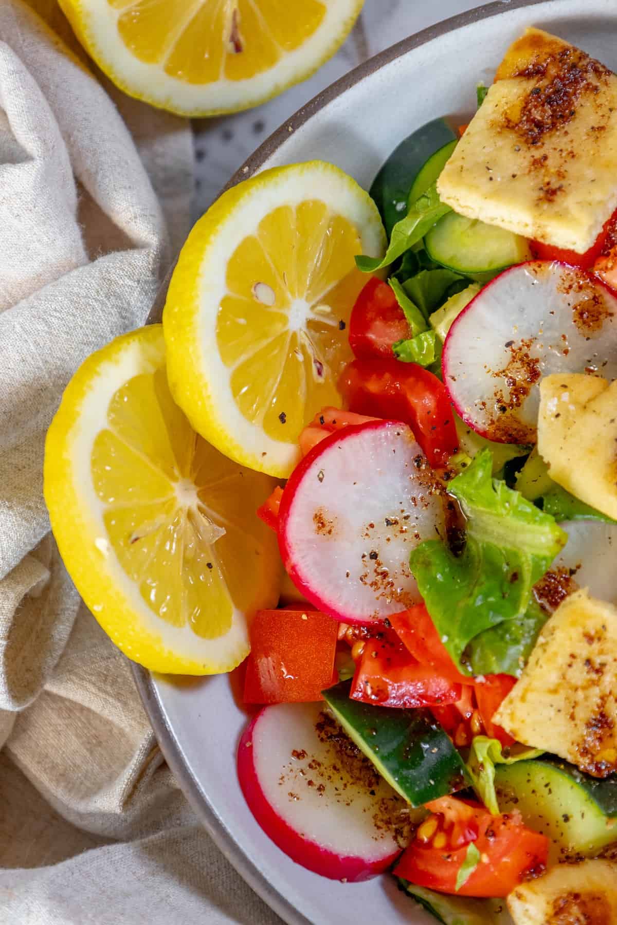 A plate of Fattoush Salad with tofu, radishes, and lemon wedges.