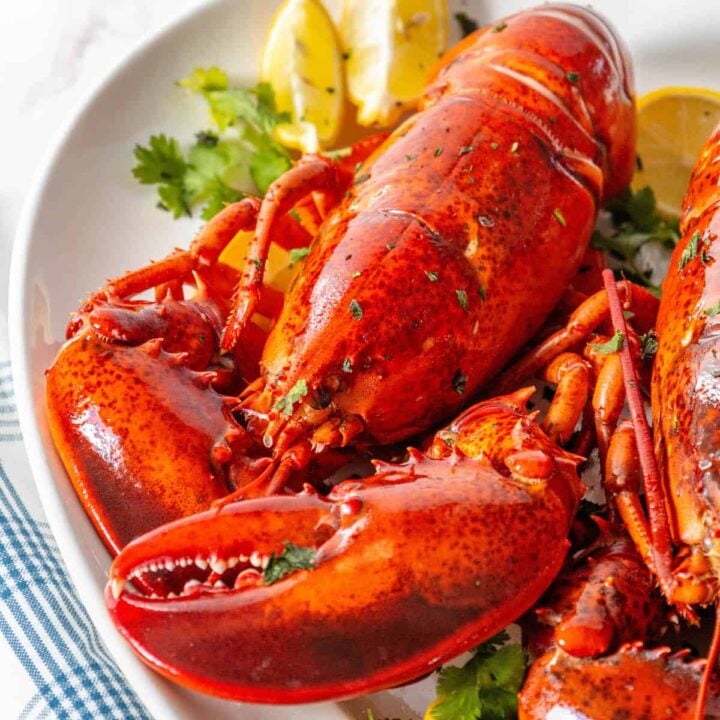 Cooked lobsters on a white plate with lemon wedges.